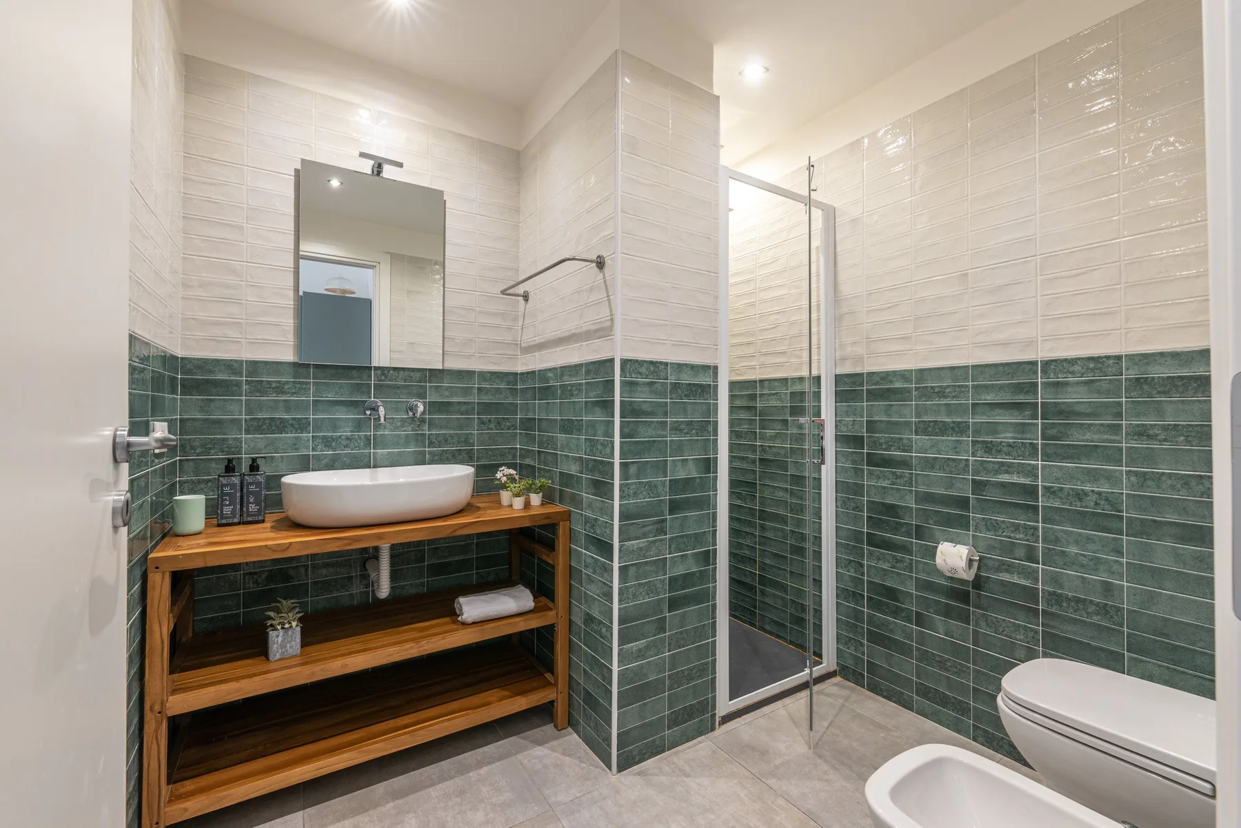 A tiled bathroom with a wooden vanity and glass shower screen.