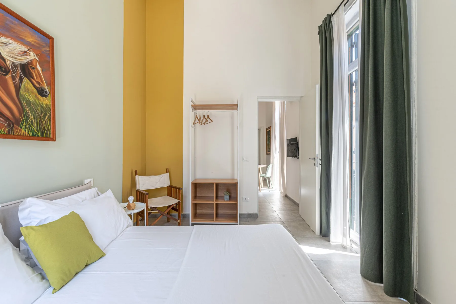 A bright bedroom with a neatly made bed and tall curtained windows.