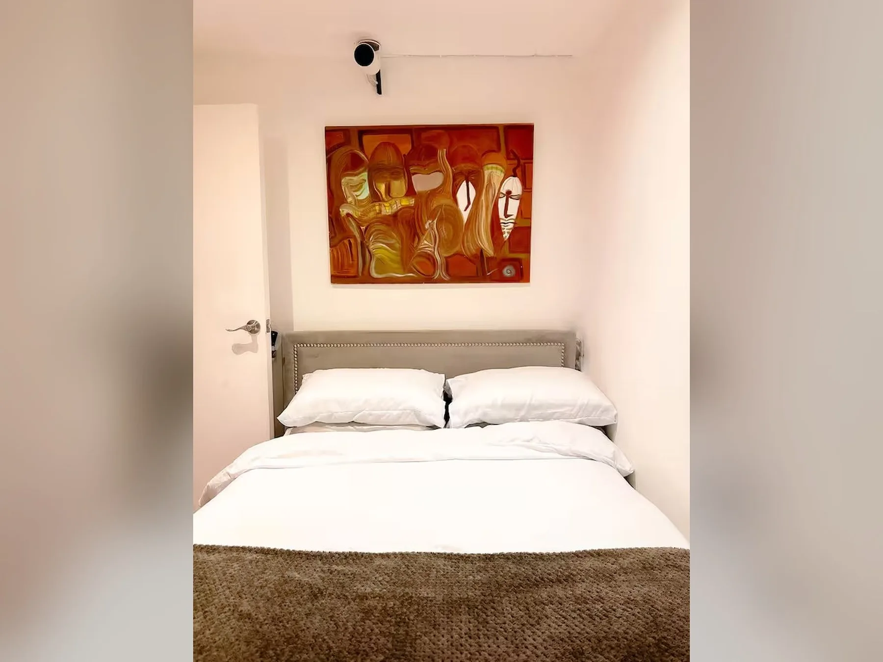 A bedroom with a neatly made bed beneath a colorful painting.
