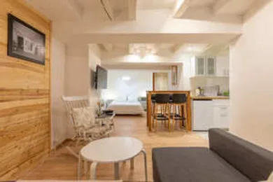 An open-plan living and dining area has a dining table, seating, and a bed in the background.