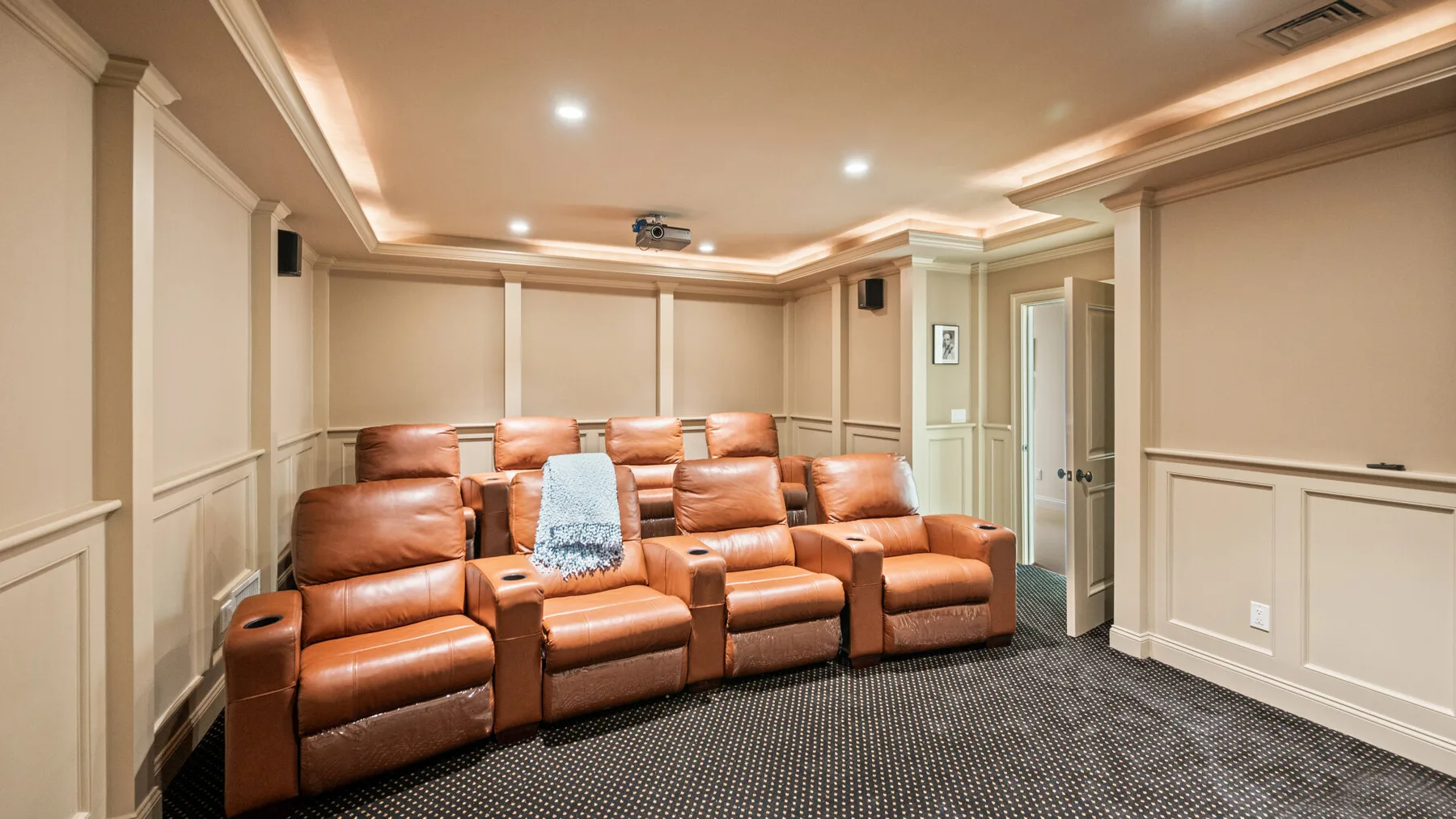 Sala de cine en casa con asientos de cuero marrón y un proyector en el techo.