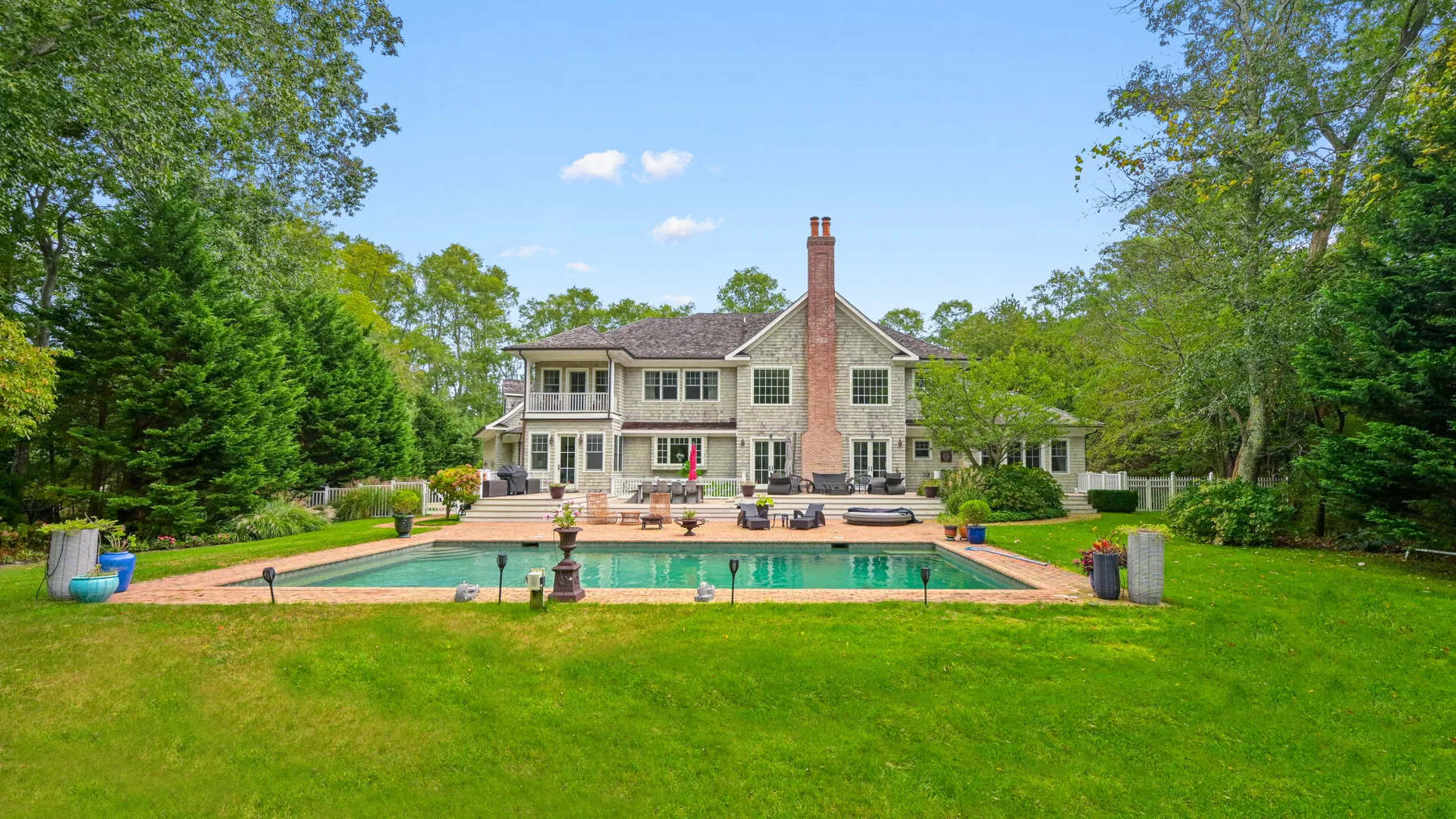A large house stands behind a swimming pool and green lawn.