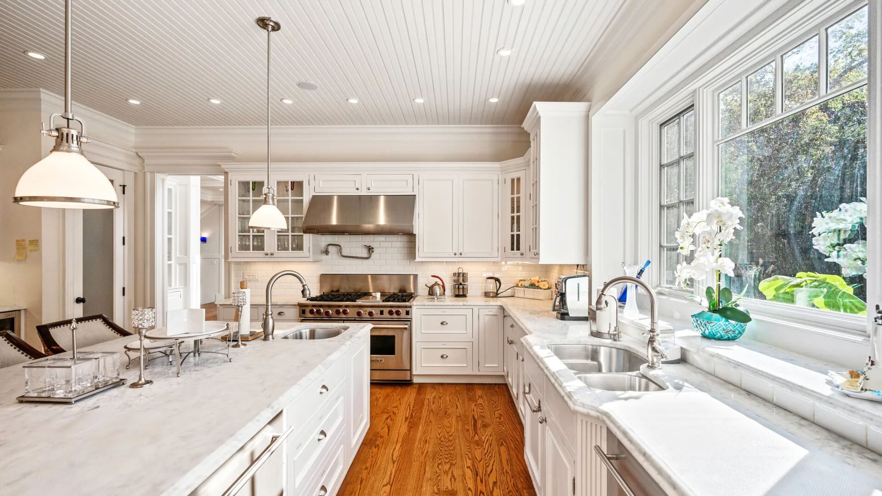 Una cocina luminosa con gabinetes blancos, una isla central y grandes ventanas.