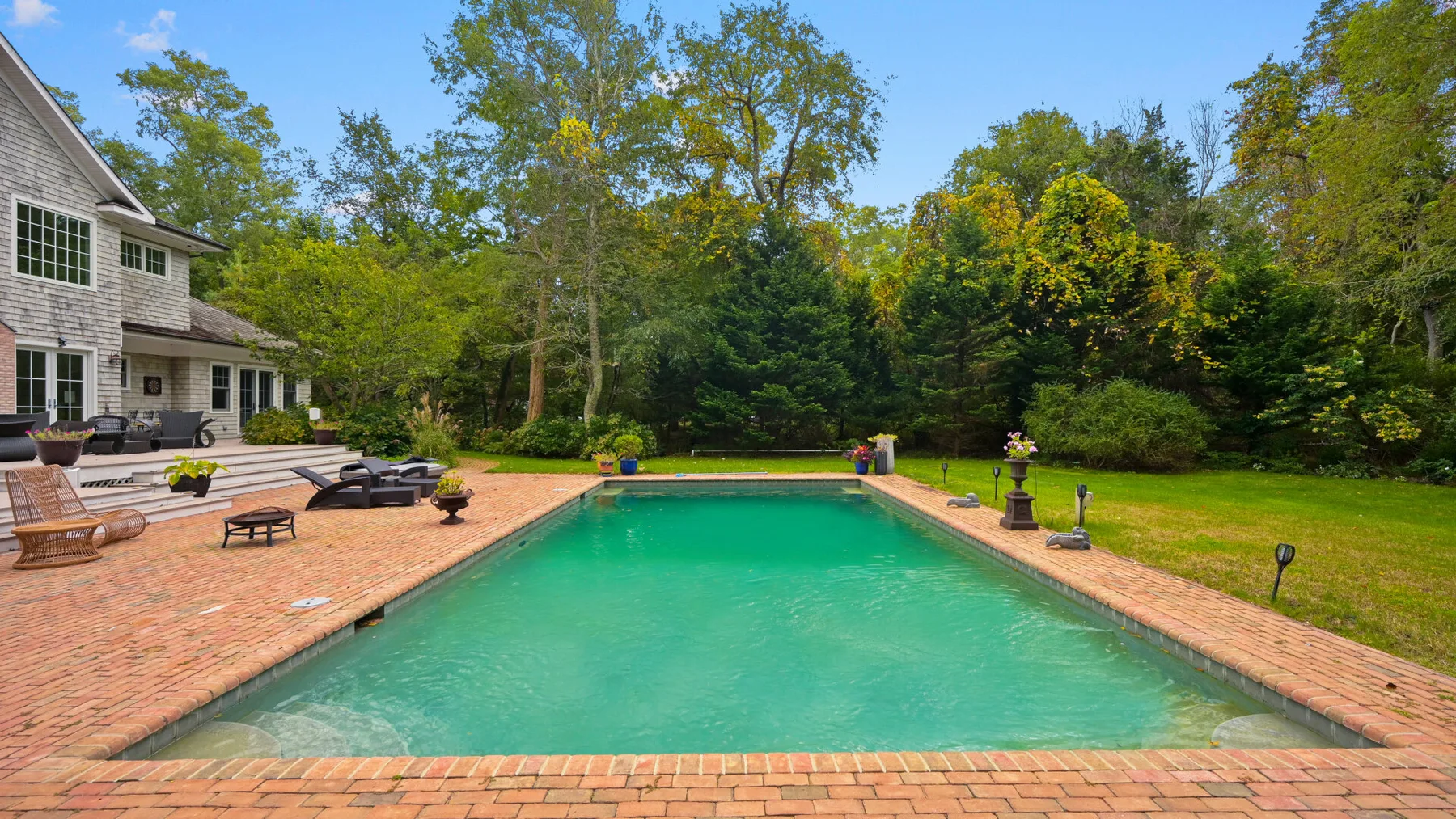 Una piscina al aire libre junto a un patio de ladrillo y una casa.