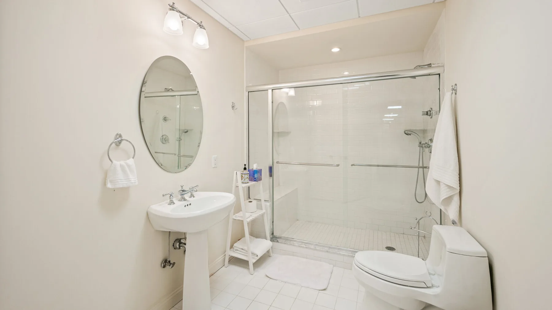 Un baño luminoso con lavabo, espejo, ducha e inodoro.