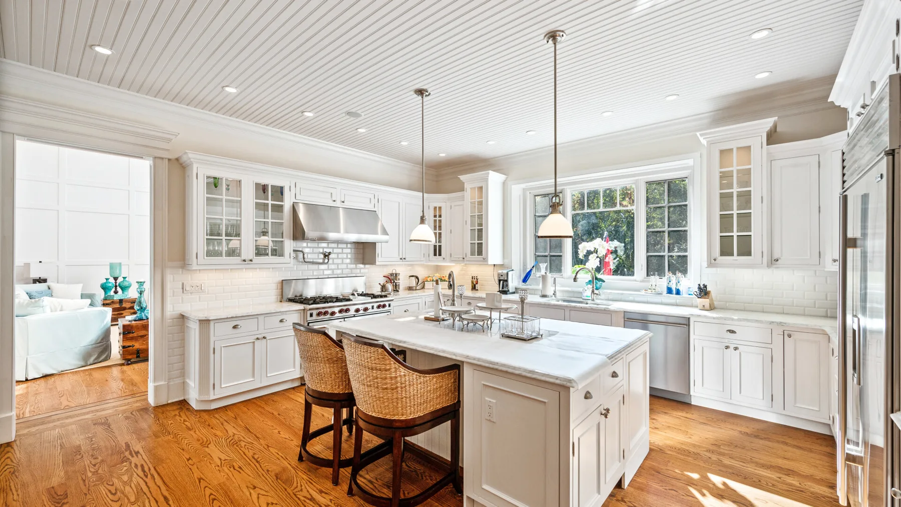 Una cocina luminosa con gabinetes blancos, una isla central y piso de madera.