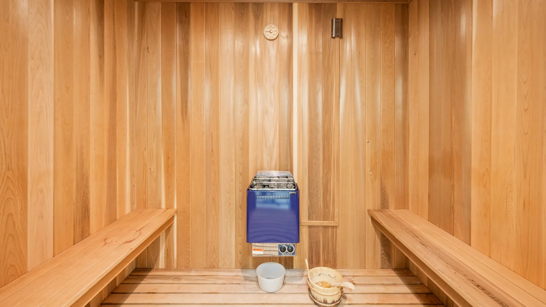 Una sauna revestida de madera con bancos junto a las paredes y una estufa.