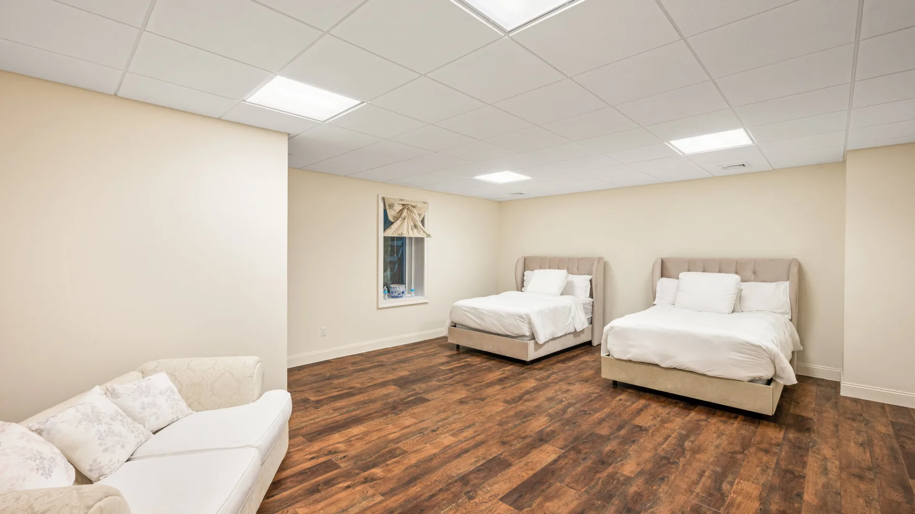 Un dormitorio con dos camas, una zona de asientos blanca y suelo con aspecto de madera.