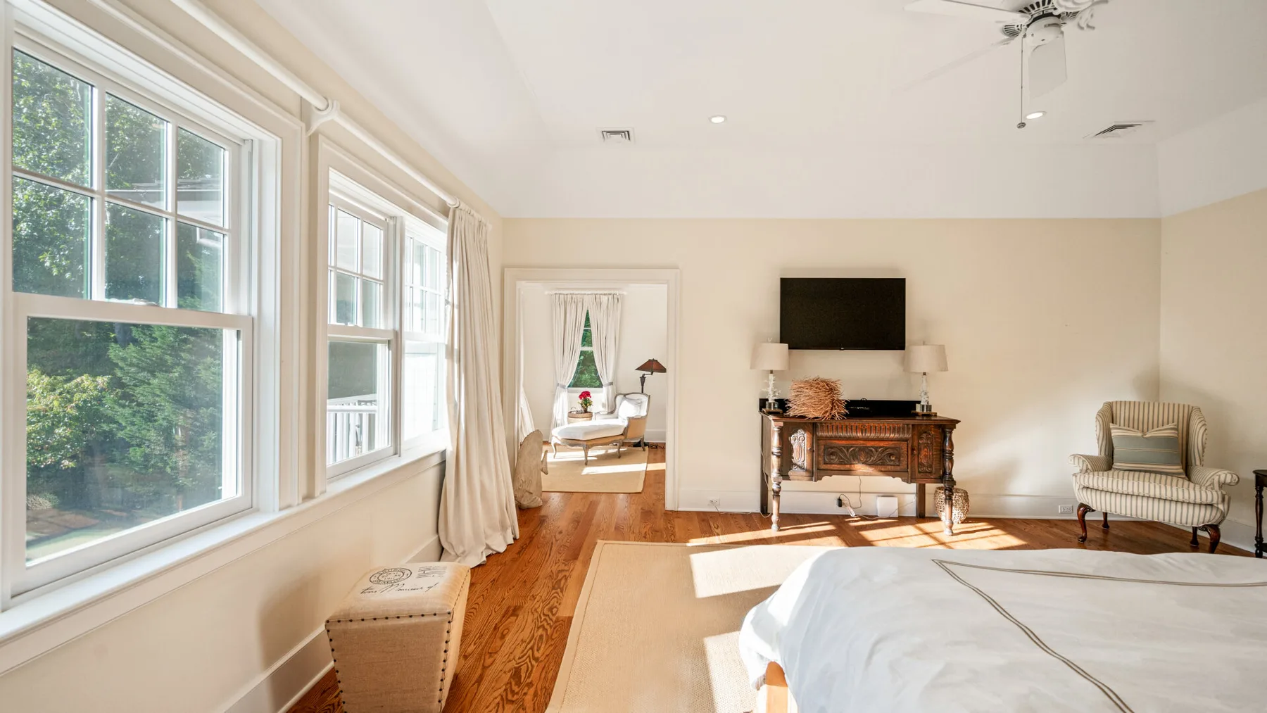 Una sala luminosa con grandes ventanas, piso de madera y un televisor.