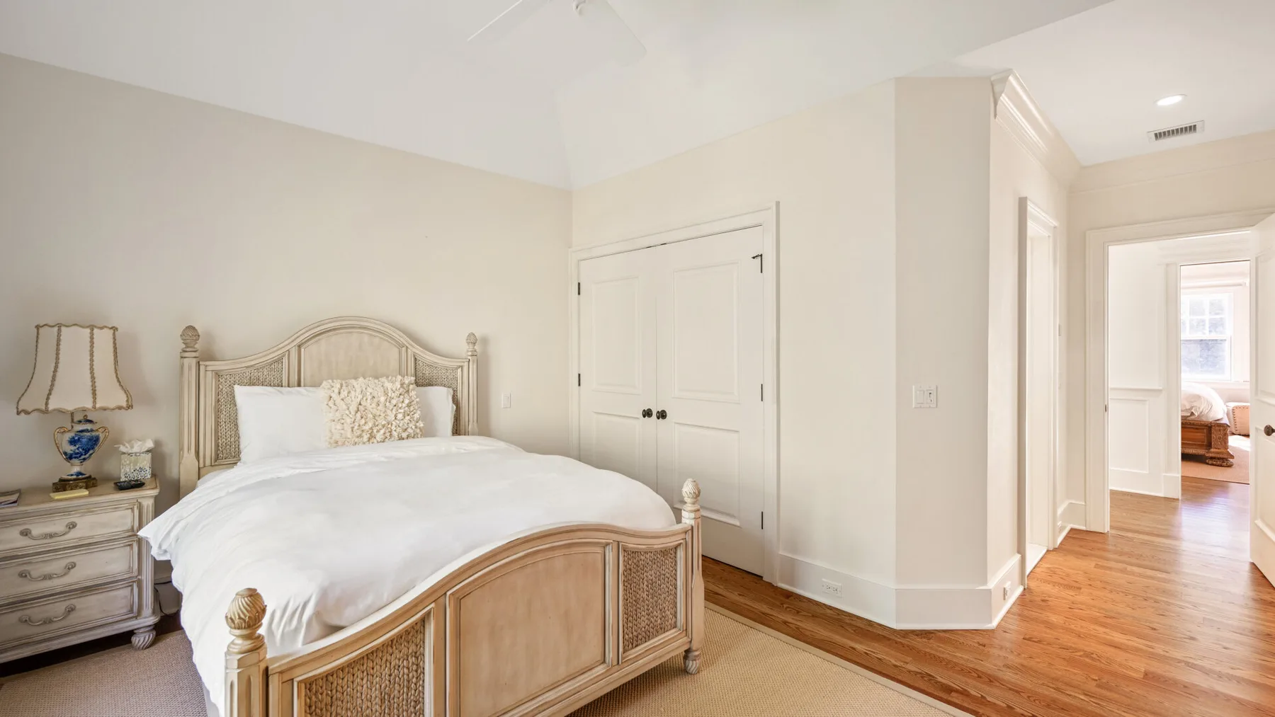 Un dormitorio luminoso con una cama de madera y un pasillo que conduce a otra habitación.