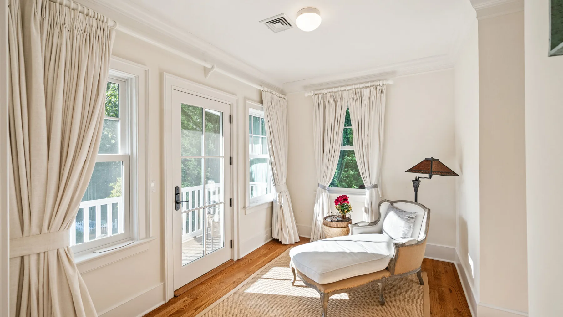 Una sala de estar luminosa tiene ventanas con cortinas, una puerta de vidrio y una chaise longue.