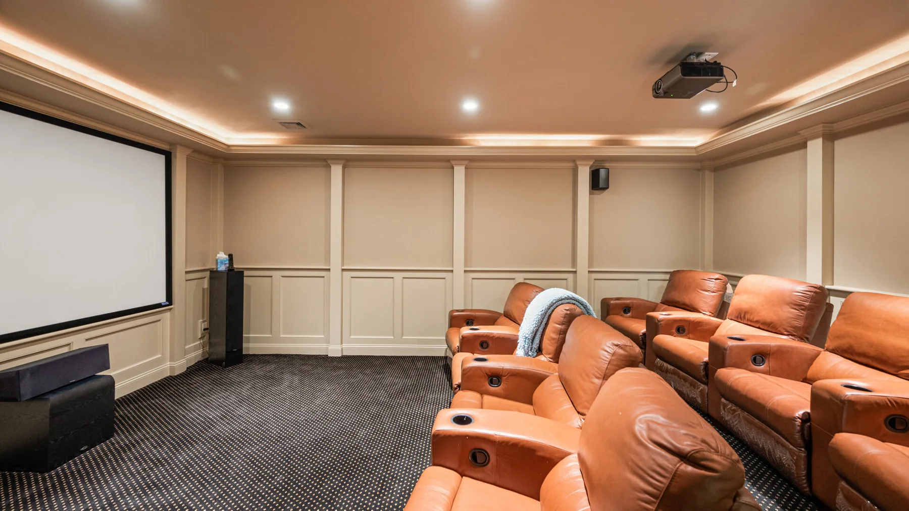 Una sala de cine en casa con asientos reclinables frente a una pantalla grande.