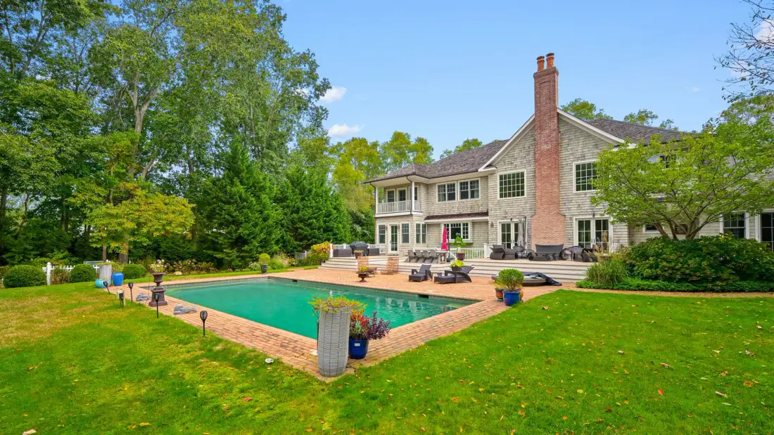 A landscaped backyard with a swimming pool beside a large house.