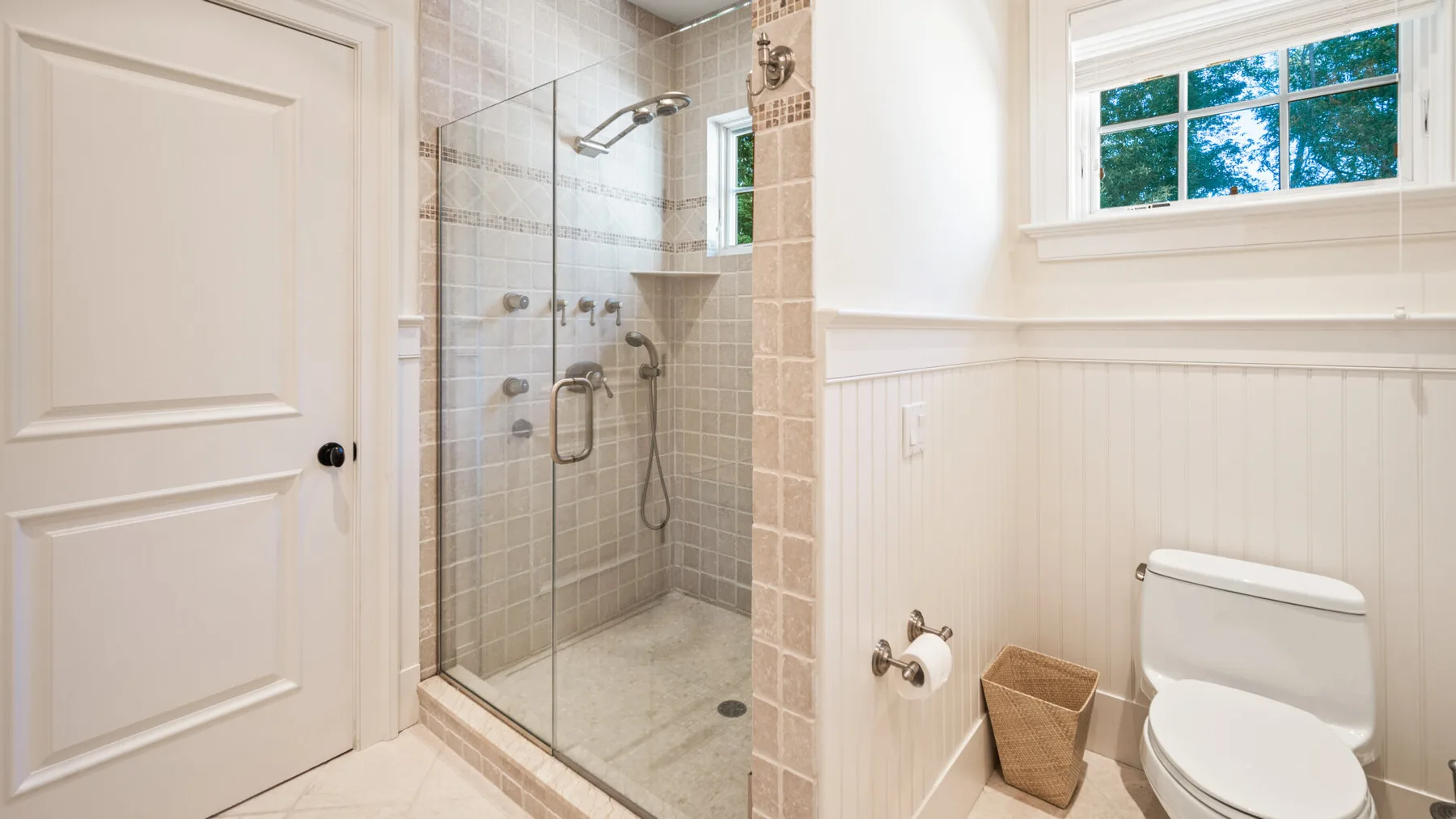 Un baño con ducha de vidrio y un inodoro junto a una ventana.