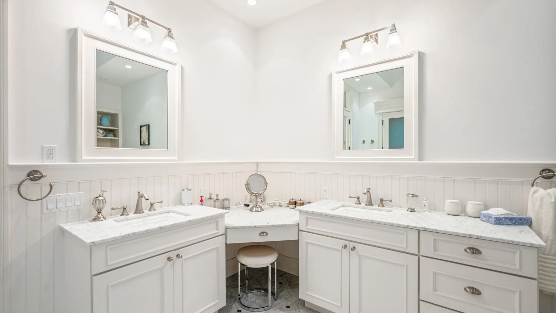 Un baño luminoso con dos lavabos, espejos y armarios blancos.