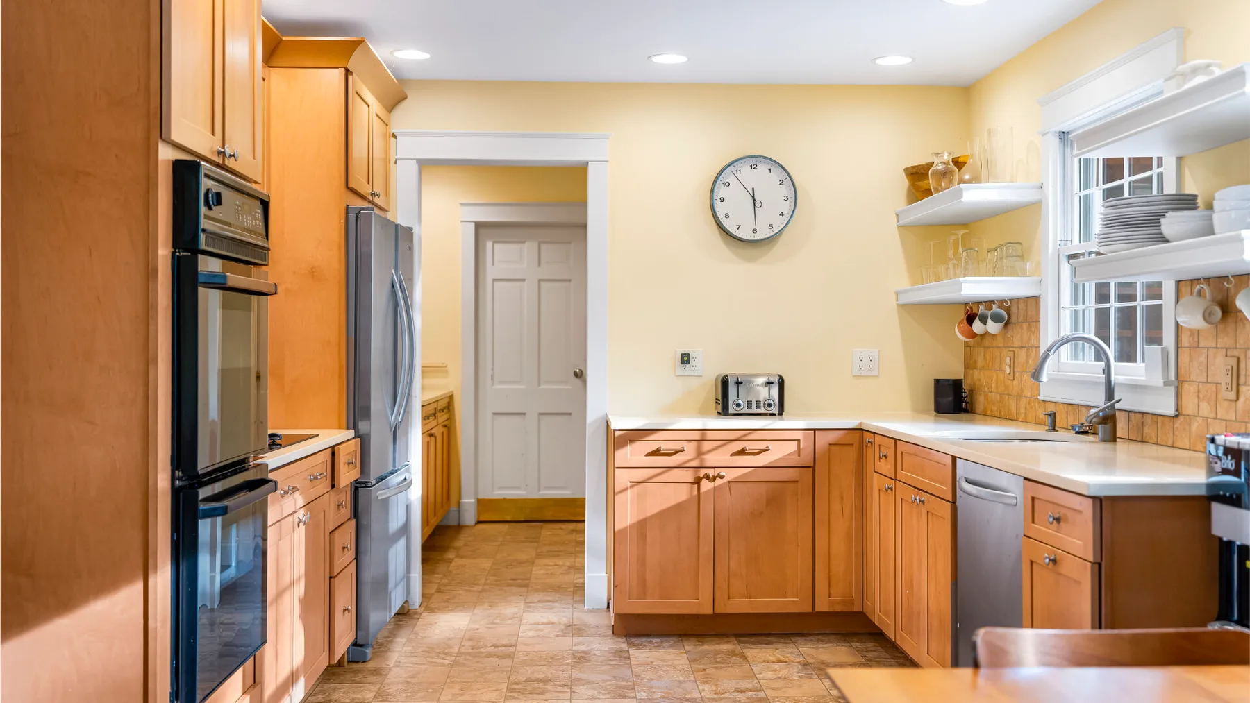 Una cocina luminosa con gabinetes de madera, electrodomésticos de acero inoxidable y piso de baldosas.