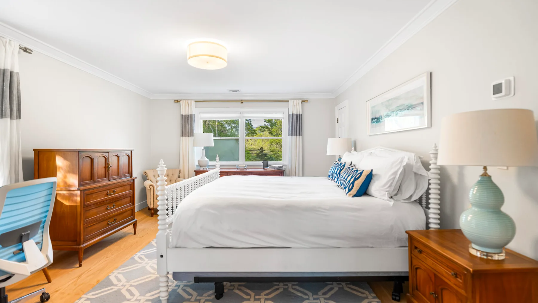 Un dormitorio luminoso con una cama grande, cómodas de madera y una ventana.