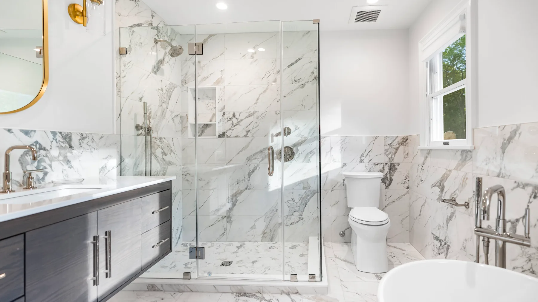 Un baño luminoso con ducha de cristal, tocador, inodoro y bañera exenta.