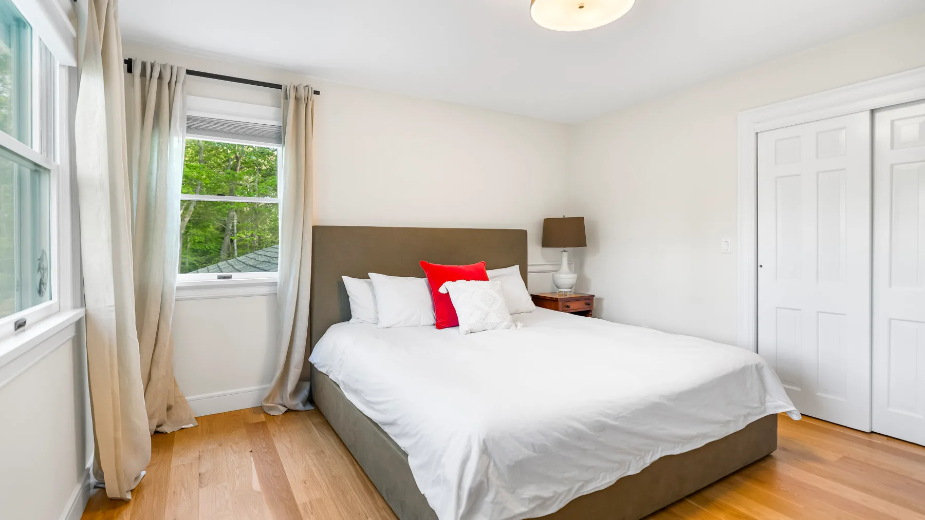 Un dormitorio con una cama junto a una ventana con cortinas claras.
