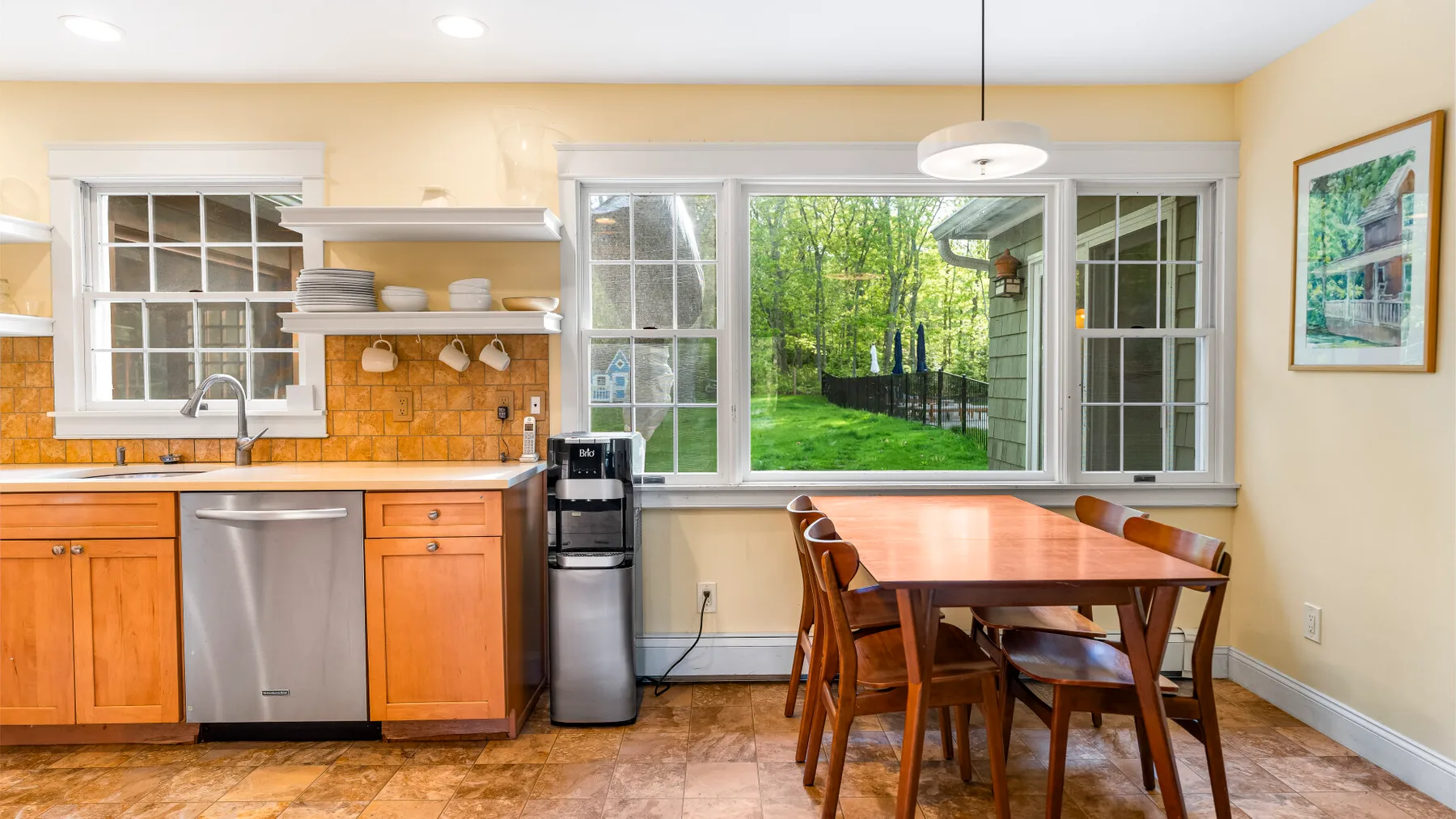 Una cocina y comedor luminosos con gabinetes de madera y una mesa junto a grandes ventanas.