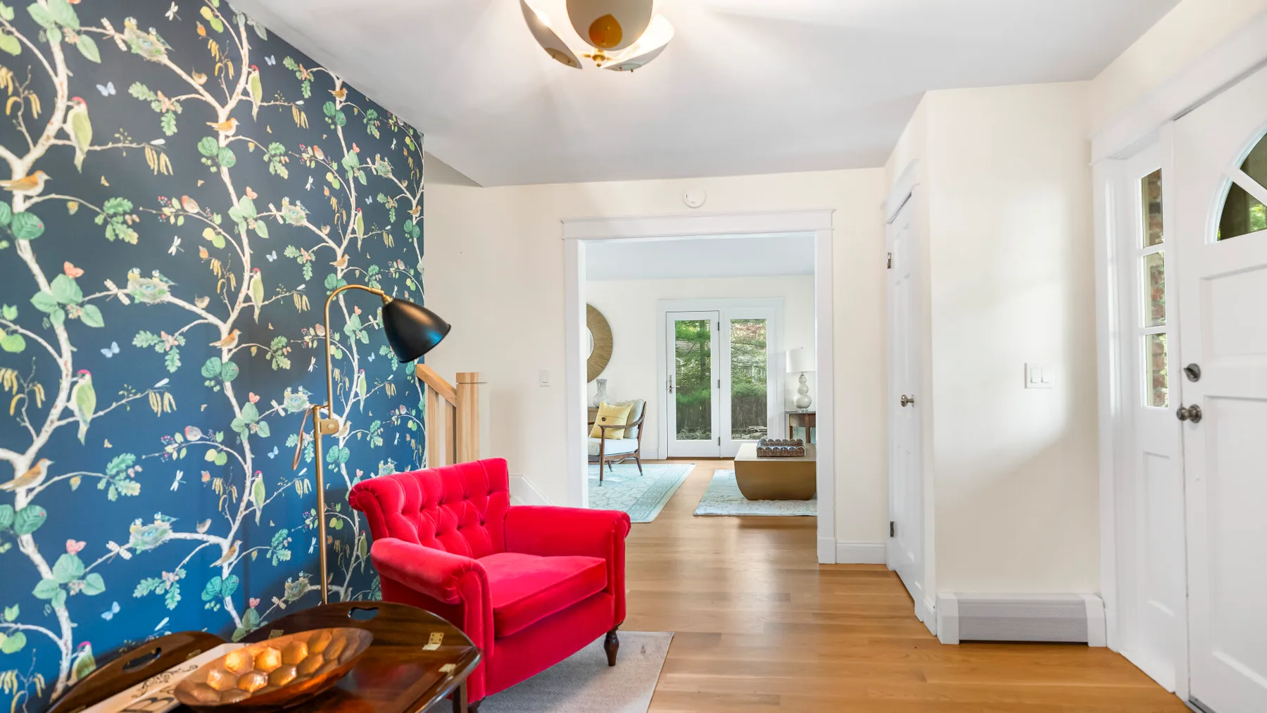 Una entrada luminosa da a una sala de estar, con un sillón rojo junto a un papel pintado estampado.