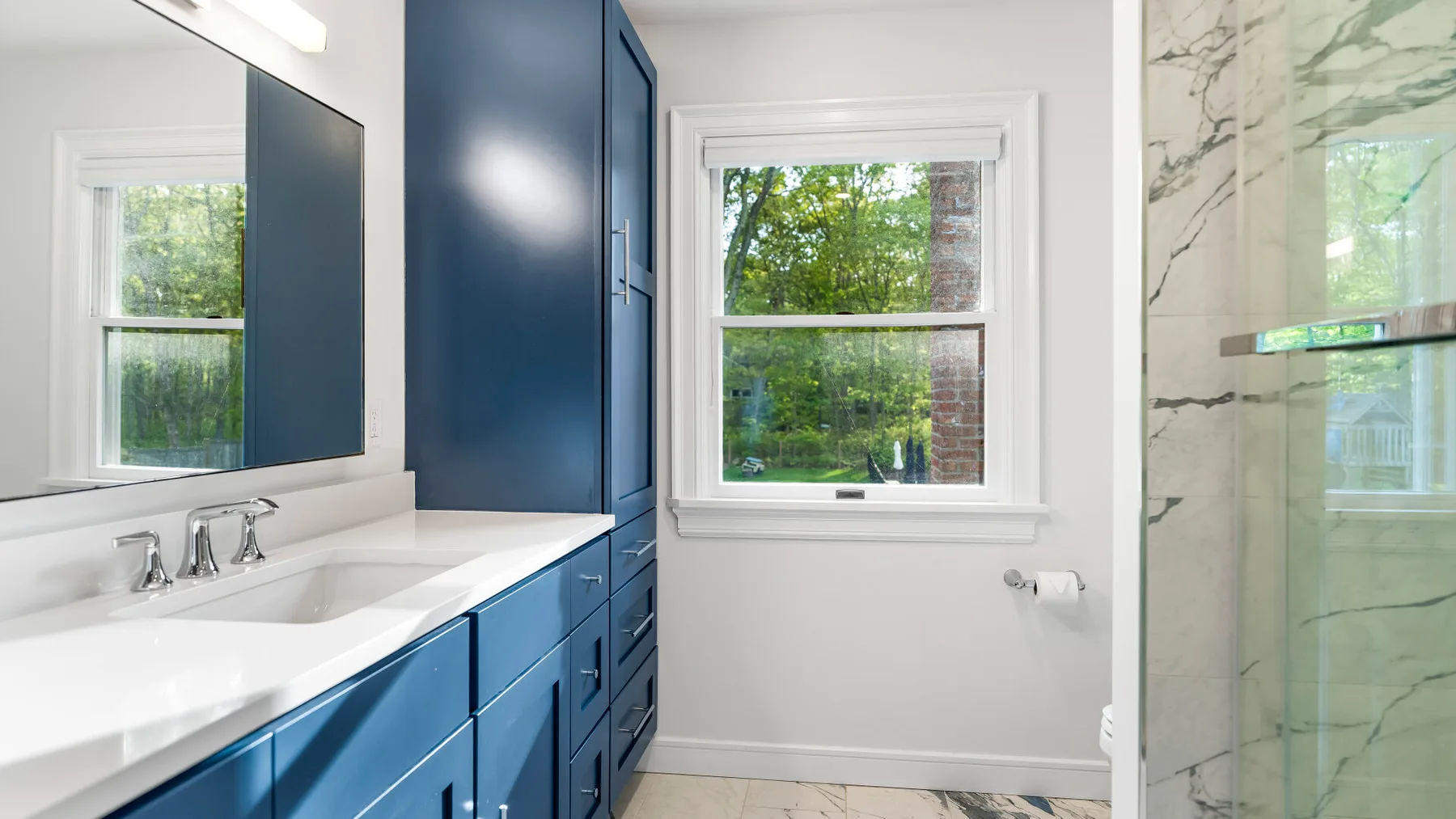 Un baño luminoso con gabinetes azules, un lavabo y una ducha de vidrio.