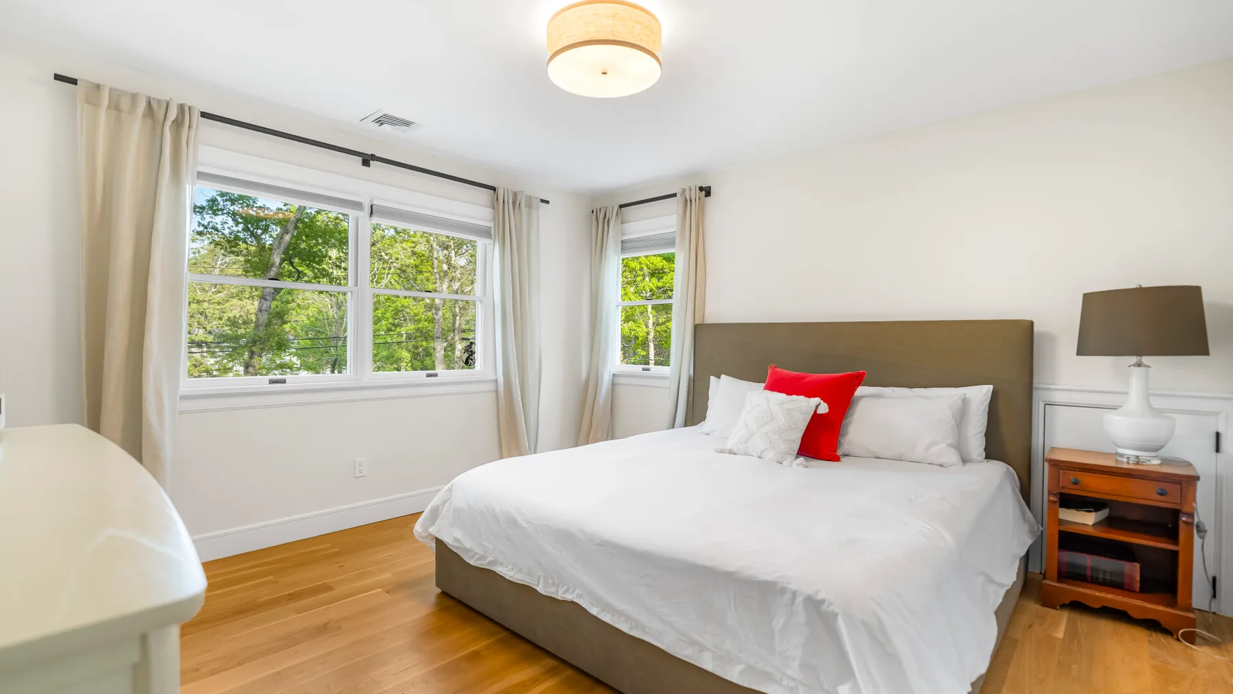 Un dormitorio luminoso con una cama bien hecha y ventanas grandes.