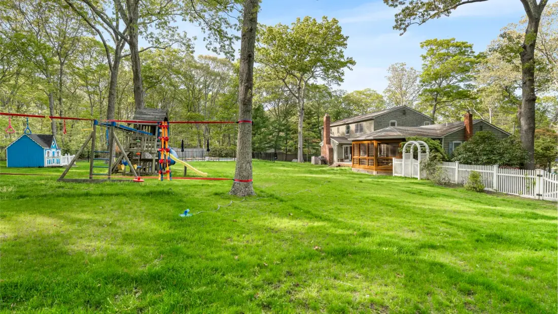 A house and children's play equipment sit in a broad green yard.