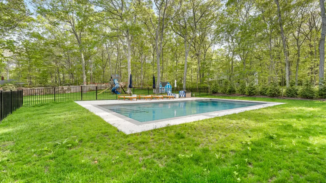 Una piscina al aire libre está en un claro con césped, rodeado de árboles.