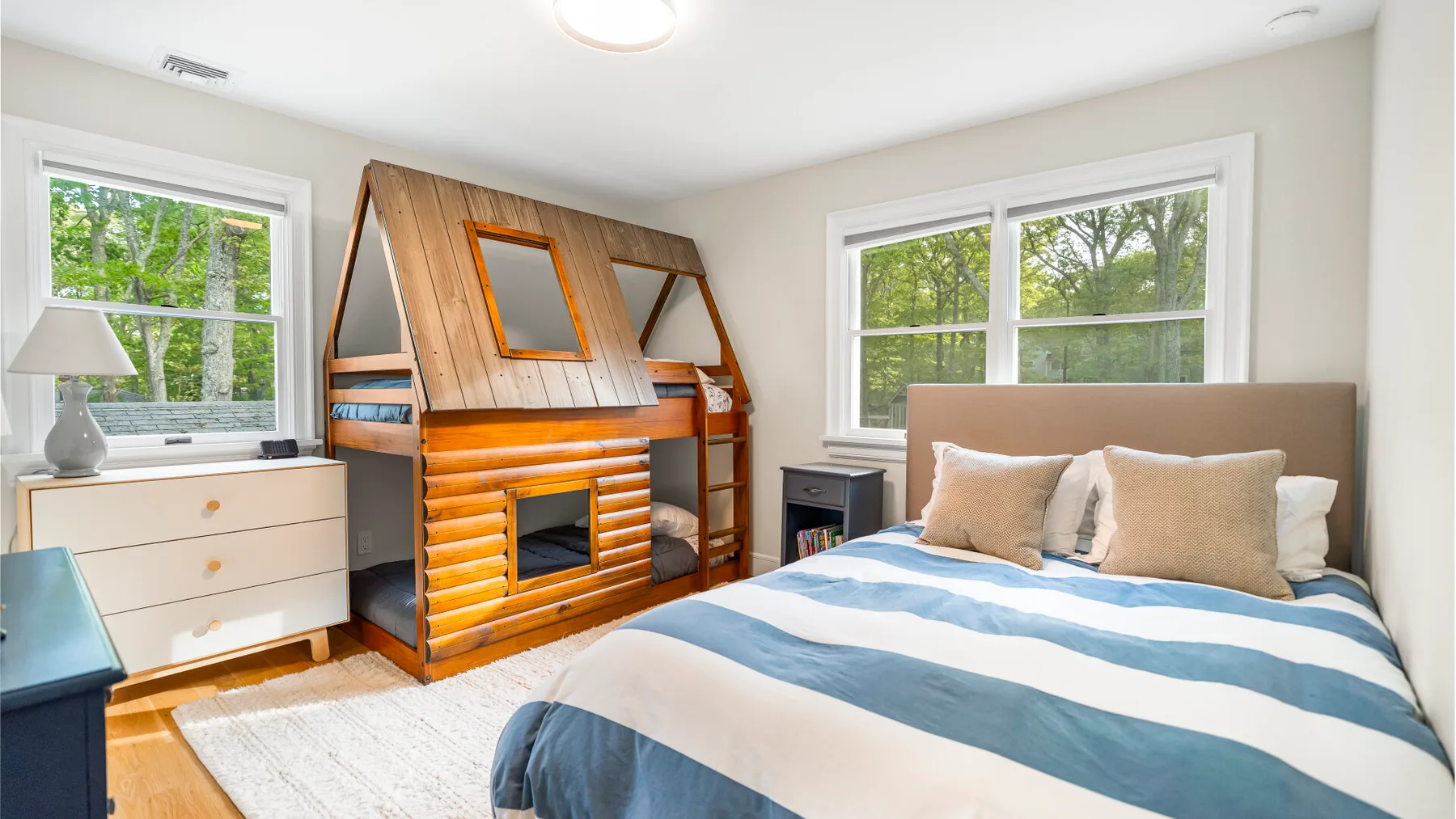 Un dormitorio con una cama y una chimenea de madera estilo cabaña bajo dos ventanas.