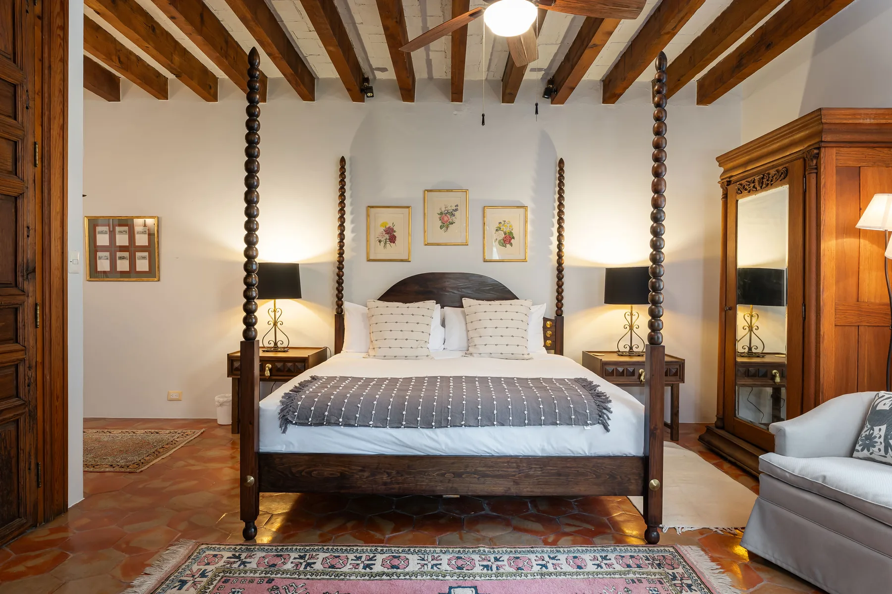 A bedroom with a large bed, exposed wooden ceiling beams, and patterned rugs.