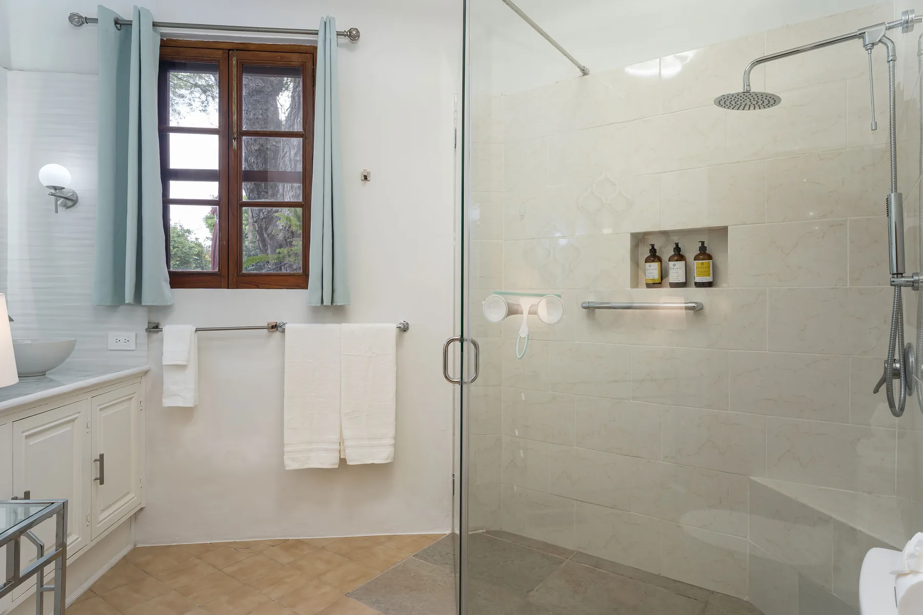 A bright bathroom with a window beside a glass shower.