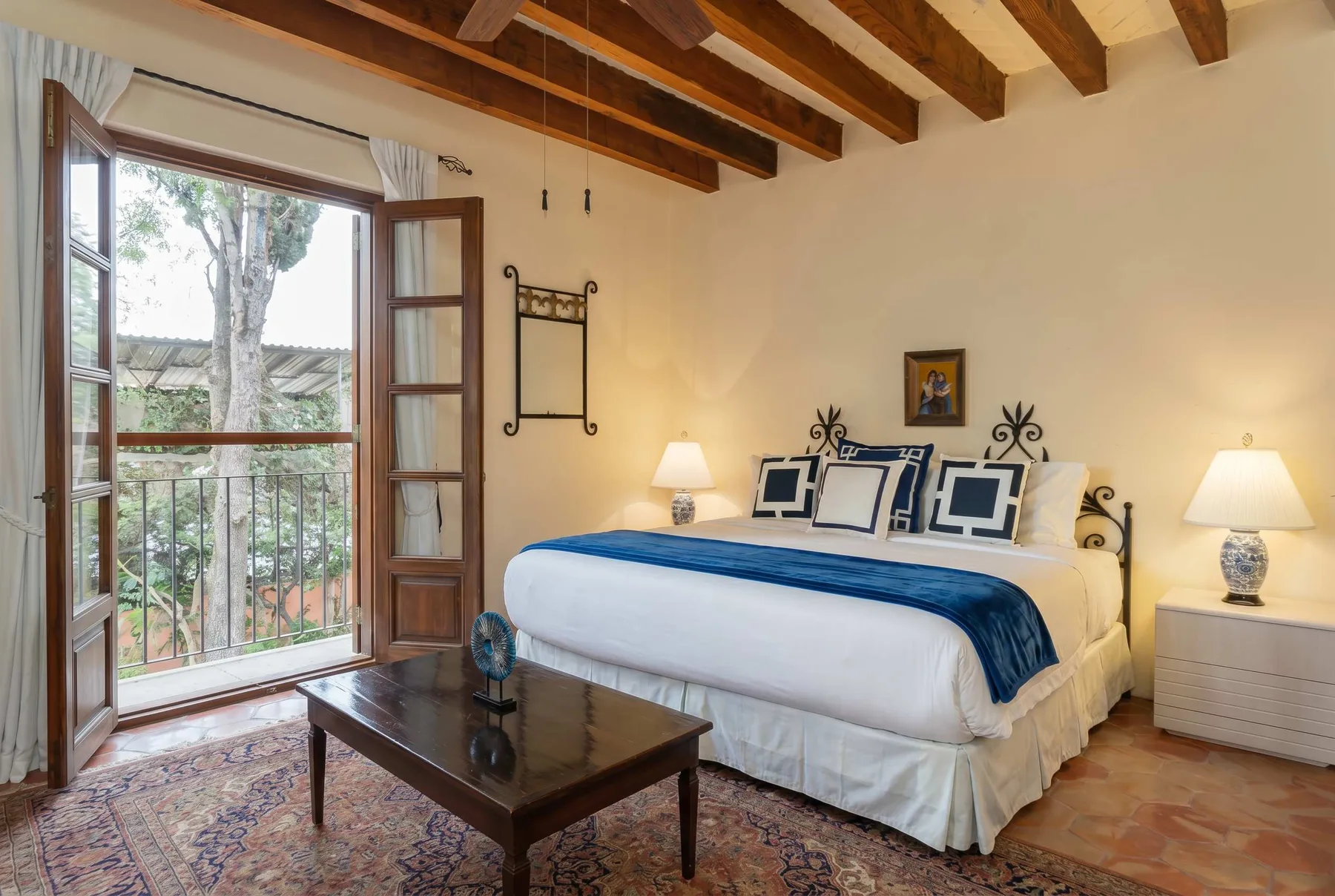A bedroom with a large bed, bedside lamps, and a window opening onto a balcony.