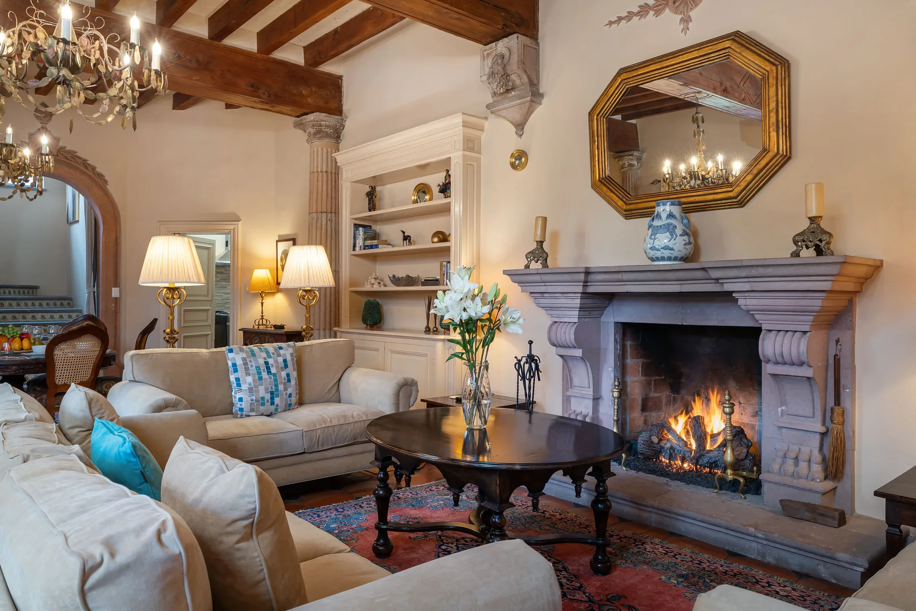 A living room with seating arranged around a table and a lit fireplace.