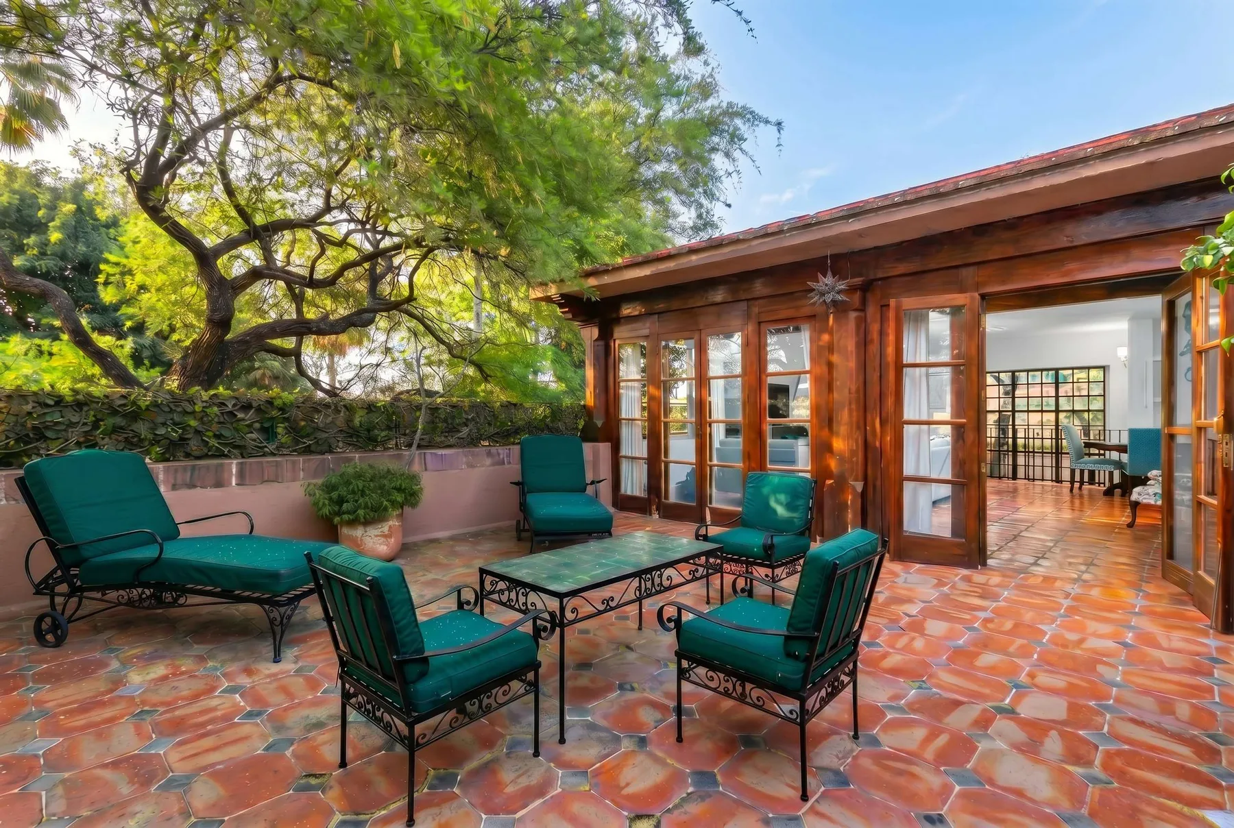 A tiled outdoor patio with green seating sits beside a wood-framed glass room.