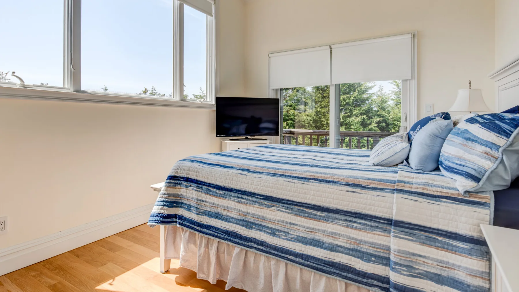 Dormitorio con una cama a rayas, ventanas grandes y un televisor.