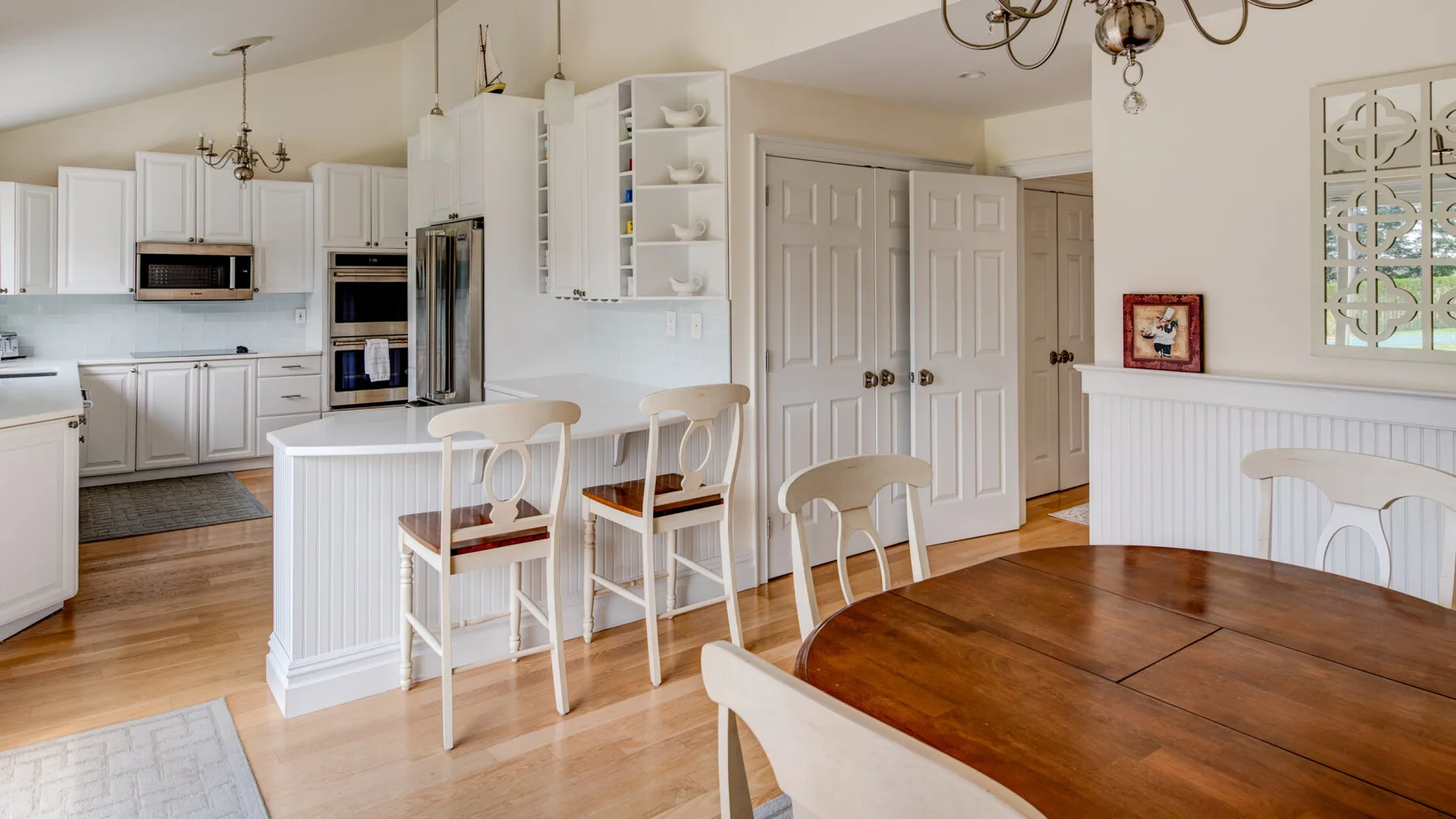 Una cocina y comedor luminosos con gabinetes blancos y una mesa de madera.