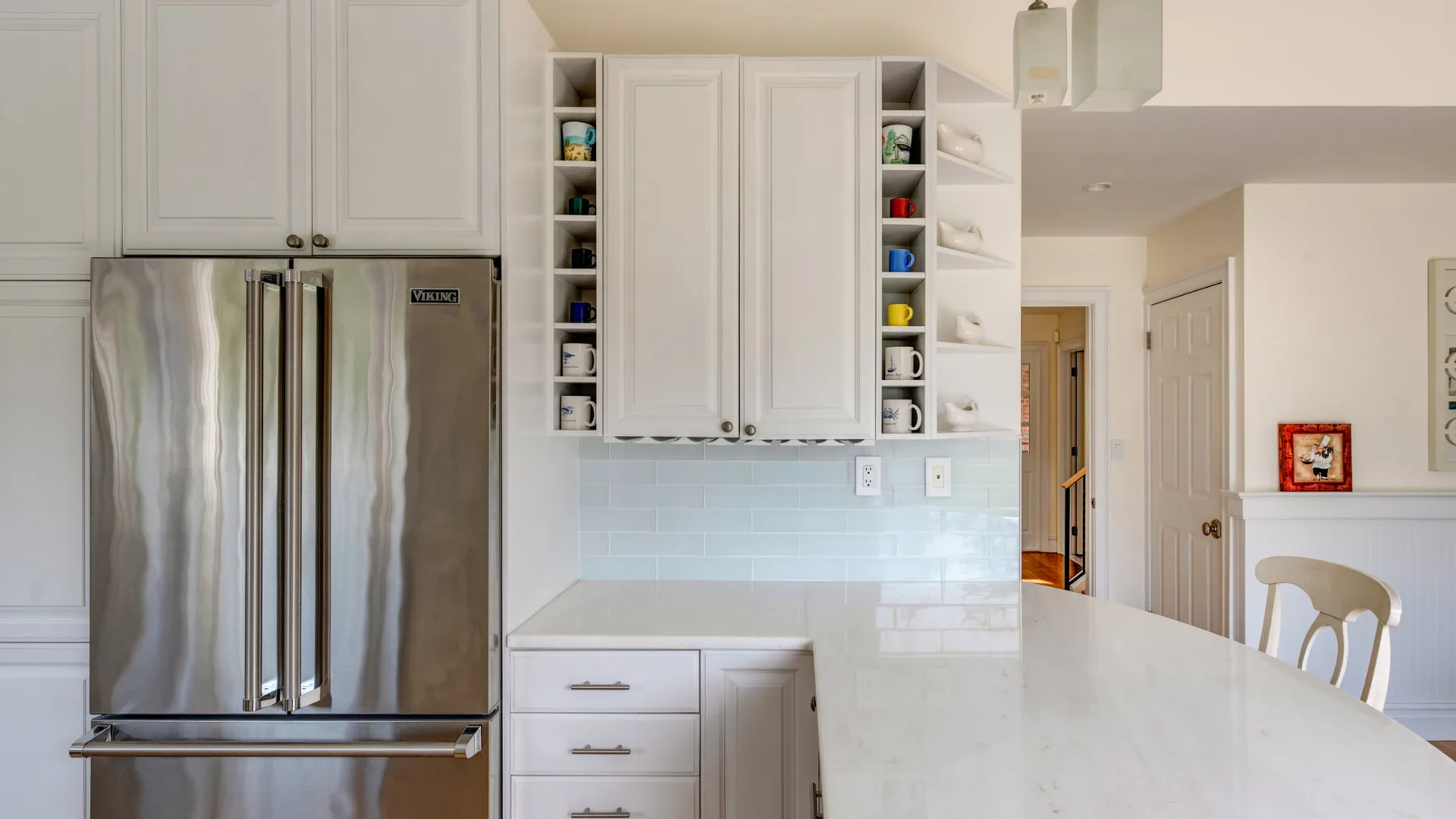 Una cocina luminosa con gabinetes blancos, un refrigerador de acero inoxidable y una isla amplia.