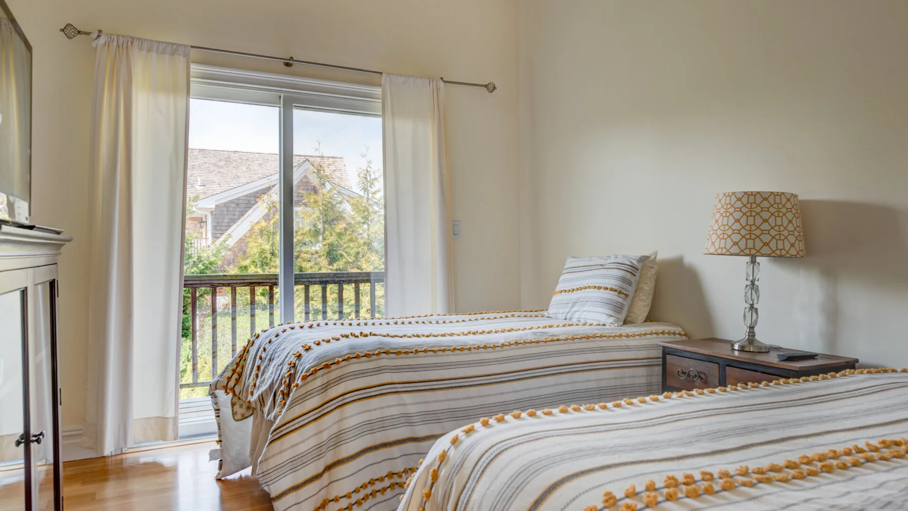 Un dormitorio luminoso con dos camas, ropa de cama a rayas y una ventana con vistas a la vegetación.