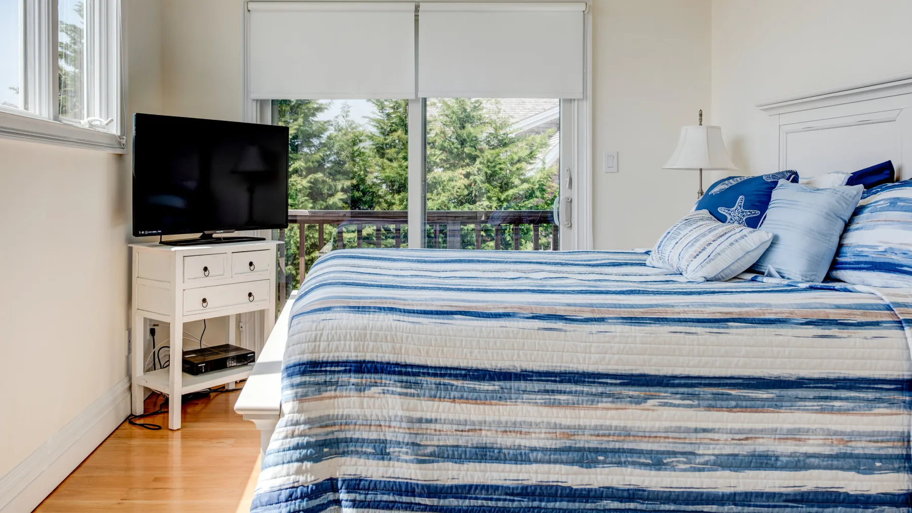 Un dormitorio luminoso con una cama de rayas azules junto a una ventana grande.