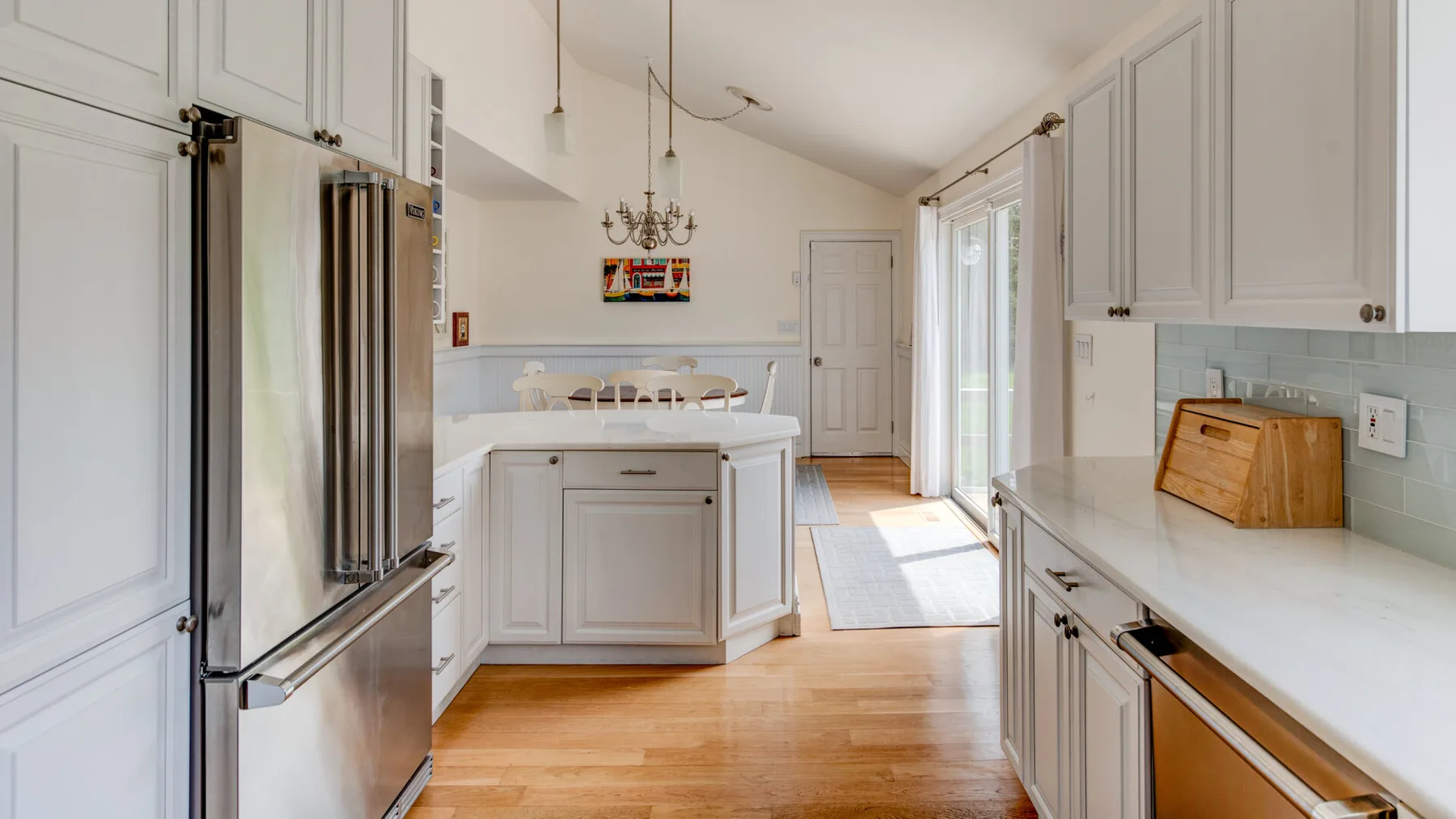 Una cocina luminosa con una isla central, un refrigerador de acero inoxidable y piso de madera clara.