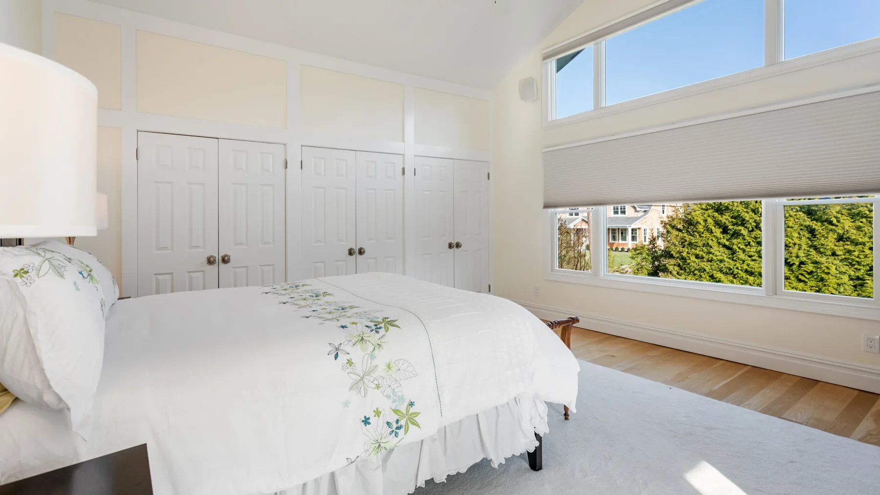 Un dormitorio luminoso con ropa de cama blanca y amplias ventanas con vistas a la vegetación.