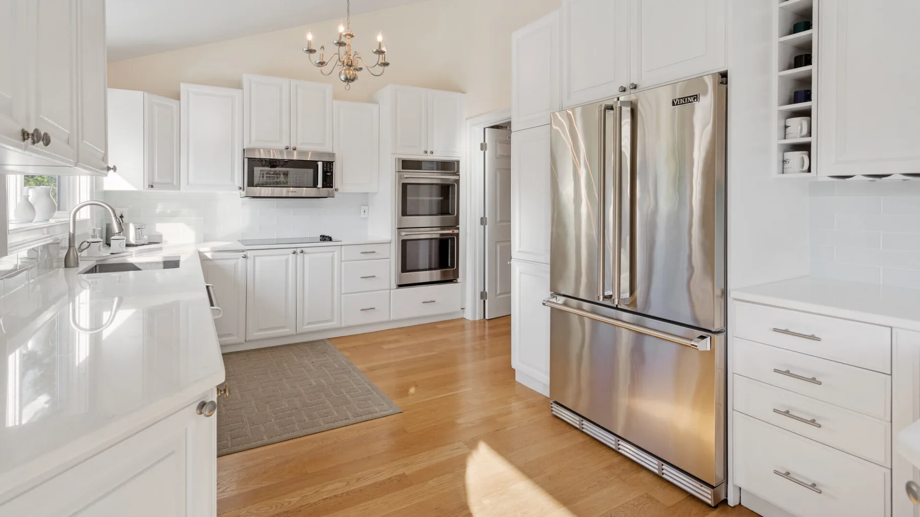 Una cocina luminosa con gabinetes blancos, refrigerador de acero inoxidable y piso de madera.