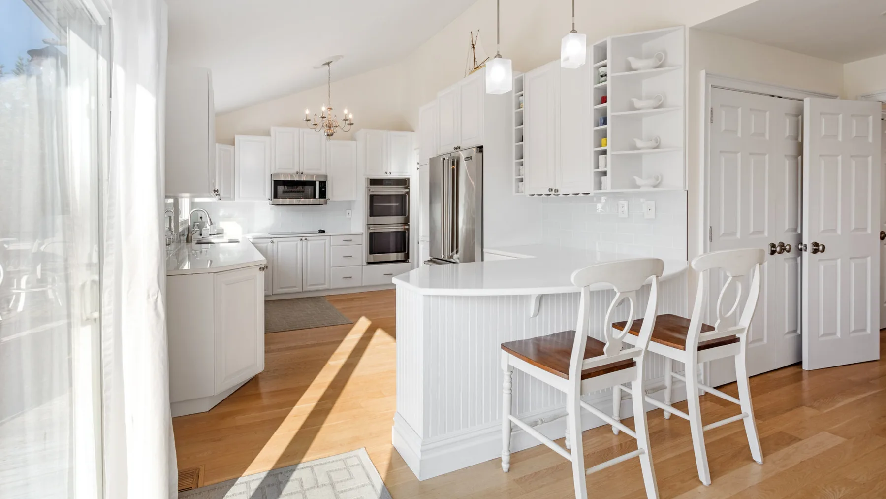 Una cocina luminosa con gabinetes blancos y una barra con asientos.