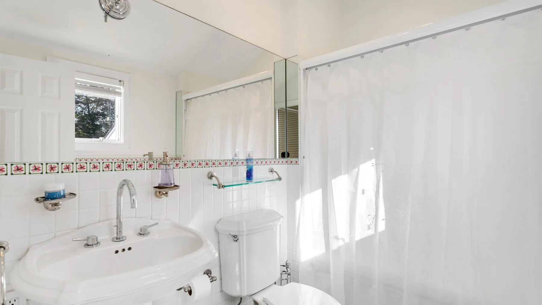 Un baño luminoso con lavabo, espejo y cortina de ducha.