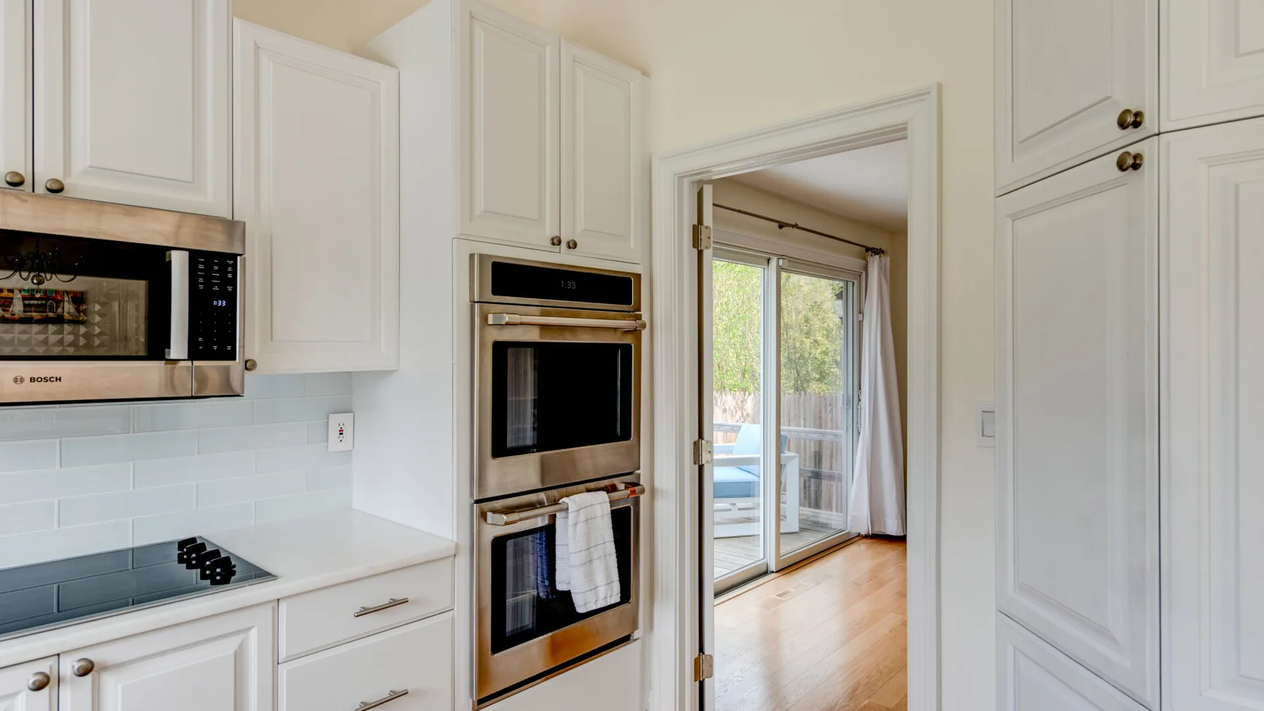 Una cocina luminosa con gabinetes blancos y una entrada a una habitación con puertas de vidrio.