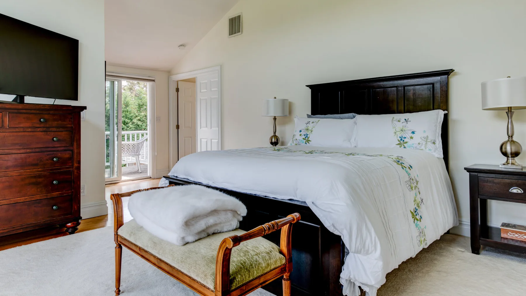 Un dormitorio con una cama vestida con ropa blanca y un banco de madera a sus pies.