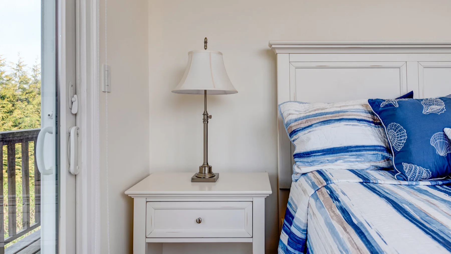 Un dormitorio con ropa de cama azul y blanca junto a una mesita y una lámpara.