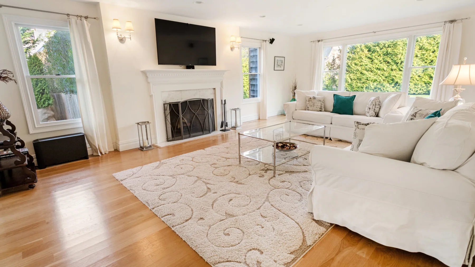 A bright living room with white seating, a fireplace, and large windows.