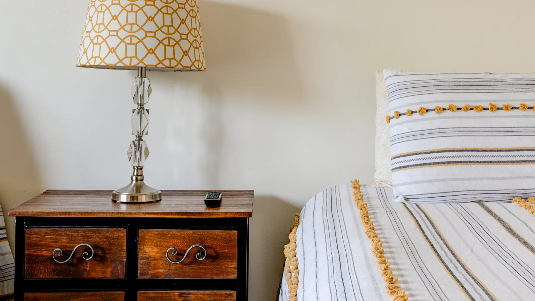 Dormitorio con una cama vestida con ropa de rayas junto a una mesita de madera.